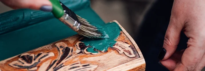 Person streicht Kommode mit grüner Farbe